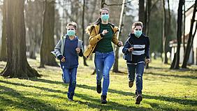 drei Jugendliche mit Maske laufen im Wald